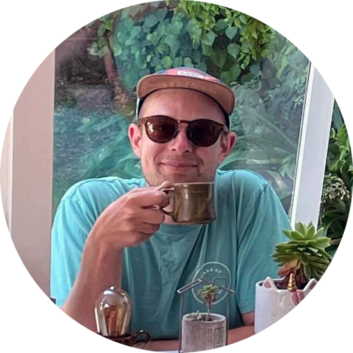 A portrait photo of Alex, smiling, holding a small cup.