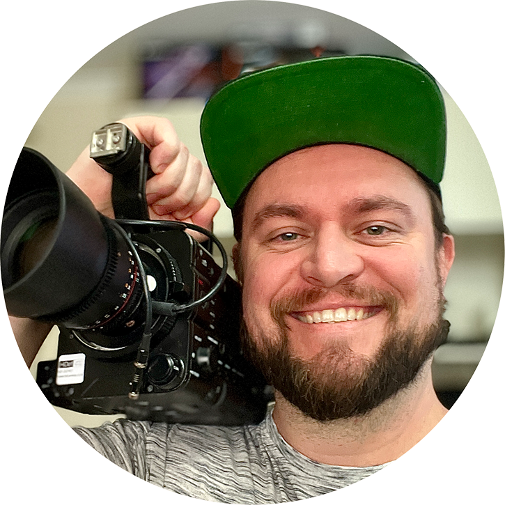 Portrait photo of Jono smiling holding a camera on his shoulder